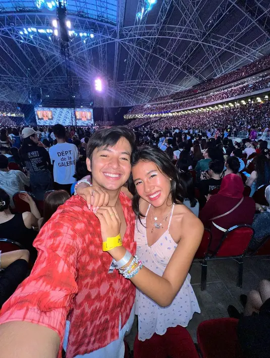 Gemasnya Angga Yunanda dan Shenina Cinnamon menonton konser Taylor Swift Bersama. Shenina tampil chic dengan mini dress putih, sedangkan Angga tampil mengenakan atasan kemeja bernuansa merah muda dan celana putih. [Foto: Instagram/sheninacinnamon]