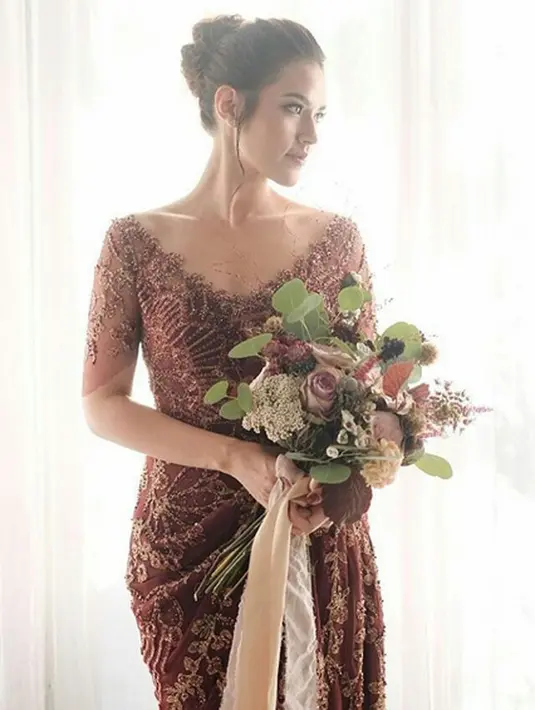 Pasangan pengantin begitu terlihat elegan dengan busana berwarna merah maroon. Terlebih dengan Raisa yang semakin terpancar aura kecantikannya dengan dress panjang dan tatanan rambut yang indah. (Instagram/_yourraisa)