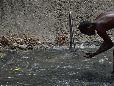 Seorang pria mengeluarkan lumpur dari dasar saluran pembuangan saat dia mencari logam berharga di Sungai Guaire, di Caracas, Venezuela (1/2). Puluhan warga mencari logam atau tembaga setiap hari di Sungai Guaire. (AFP Photo/Federico Parra)