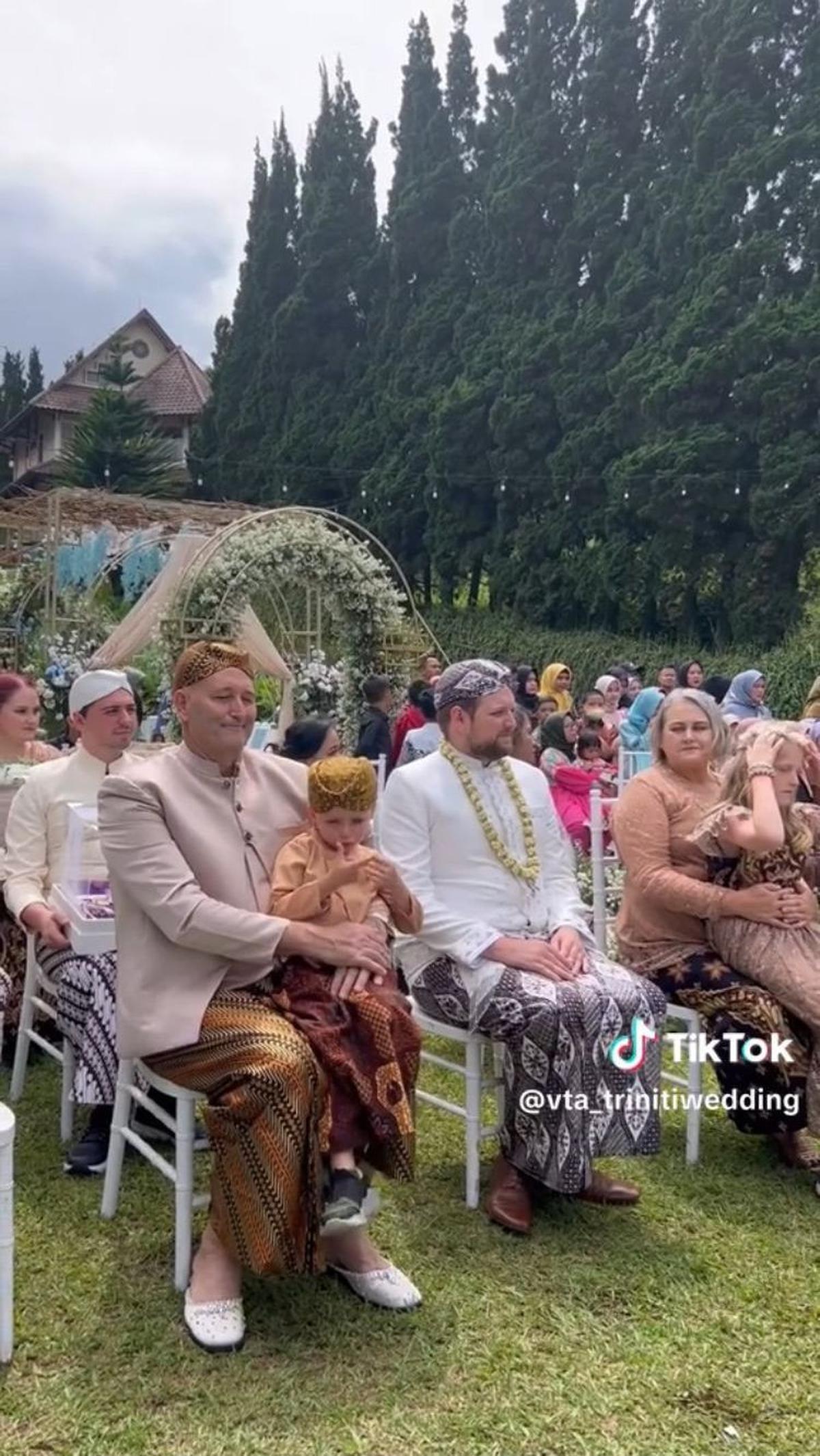 Usai dipakaikan kalung melati, mereka duduk di tempat yang sudah disiapkan untuk mempelai pria dan keluarganya.