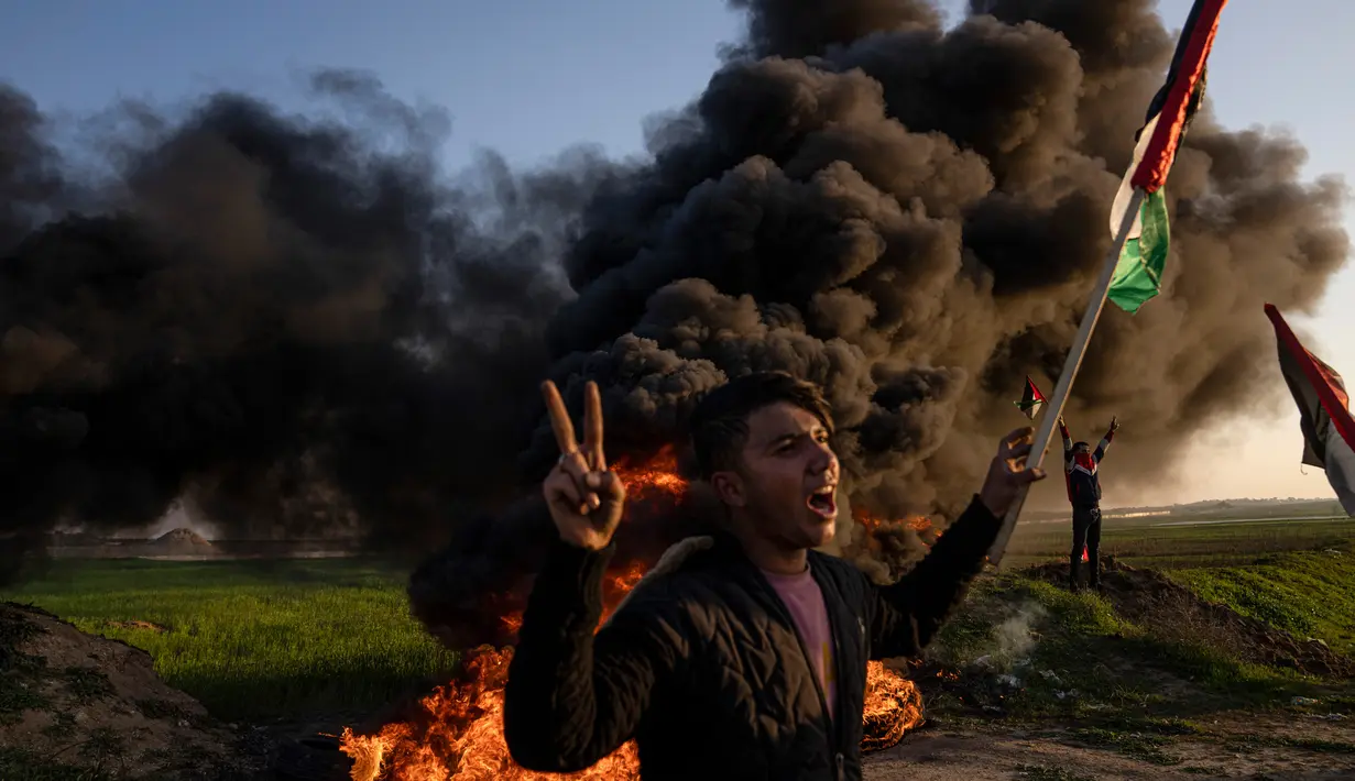 Warga Palestina membakar ban dan mengibarkan bendera nasional saat protes terhadap serangan militer Israel terhadap kamp pengungsi Jenin di perbatasan Israel-Palestina, sebelah timur Kota Gaza, 26 Januari 2023. Brigade Martir Al Aqsa, milisi bersenjata yang berafiliasi dengan Fatah mengatakan, salah satu anggotanya bernama Izz al-Din Salahat turut menjadi korban tewas. (AP Photo/Fatima Shbair)