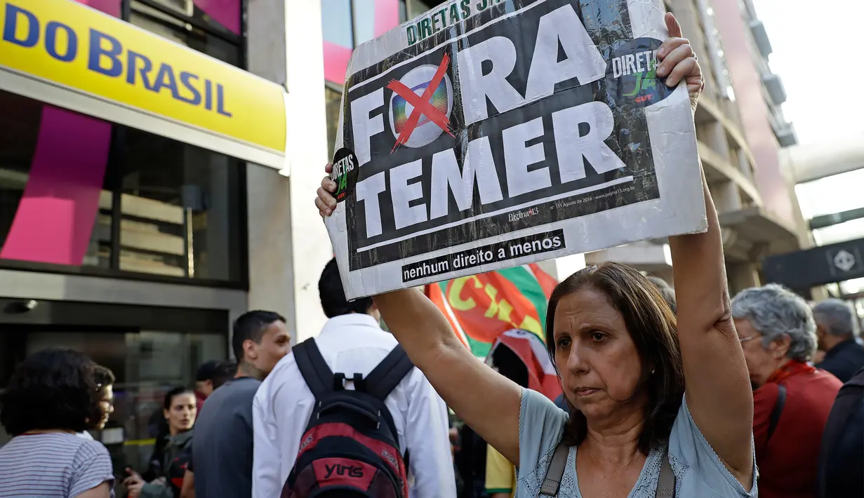 Seorang wanita membawa poster bertuliskan “Keluarkan Temer!” dalam unjuk rasa di Sao Paulo, Brasil, Rabu (2/8). Demonstrasi tersebut bertujuan untuk melengserkan Presiden Brasil Michel Temer yang diduga terkait kasus korupsi. (AP/Andre Penner)