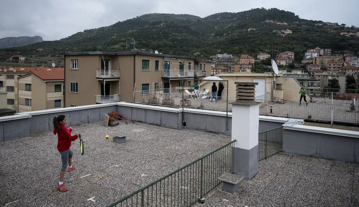 Carola Pessina bermain tenis dengan Vittoria Oliveri di atas atap rumah mereka selama lockdown COVID-19 di Finale Ligure, Wilayah Liguria, Italia (19/4/2020). Setiap hari Carola, 11, dan Vittoria, 13, bermain tenis dari satu atap ke atap lain di rumah mereka untuk berlatih. (AFP/Marco Bertorello)