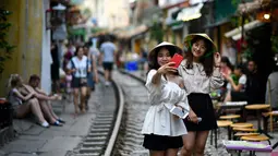 Foto pada 8 Juni 2019 menunjukkan dua orang wanita berswafoto di tengah jalur kereta api populer di Hanoi, Vietnam. Turis sengaja datang ke Old Quarter untuk berfoto di rel kereta api yang dianggap ' instagramable' tersebut. (Photo by Manan VATSYAYANA / AFP)