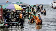 Petugas PPSU membersihkan sampah saat terjadi banjir rob di Pelabuhan Kali Adem, Muara Angke, Jakarta, Selasa (9/11/2021). Walau terendam banjir rob, petugas PPSU tetap sigap bersihkan sampah yang mengambang terbawa air laut. (Liputan6.com/Faizal Fanani)