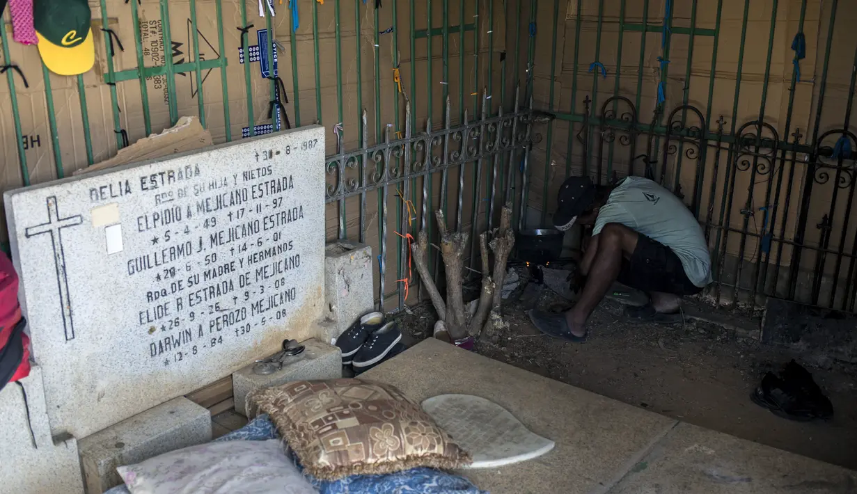 Luis Miguel Mendez dari Venezuela, 41, memasak di tempat perlindungan darurat di Pemakaman Umum Selatan di Caracas, pada 16 Februari 2021. Makam yang dirusak telah menjadi rumah bagi banyak tunawisma di Venezuela. (Pedro Rances Mattey / AFP)