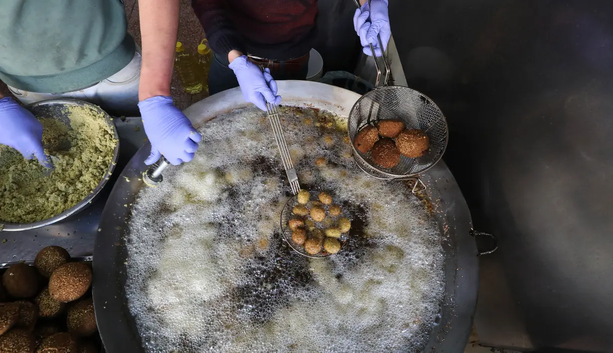 Juru masak Palestina mengenakan sarung tangan dan masker saat menggoreng falafel di sebuah restoran lokal di kota Hebron, Tepi Barat yang diduduki pada 29 April  2020. Falafel merupakan hidangan khas Palestina yang terbuat dari bahan utama kacang arab atau kacang fava. (HAZEM BADER / AFP)