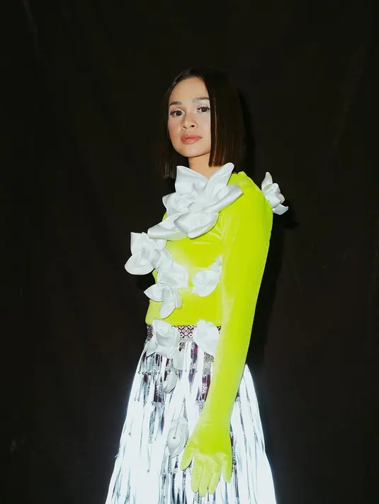 Ia mengenakan atasan warna hijau neon dengan aksen bunga putih. Atasan tersebut dipadukan rok songket dengan aksen fringe yang memberi kesan playful dan modern. [Instagram/andienmusic]
