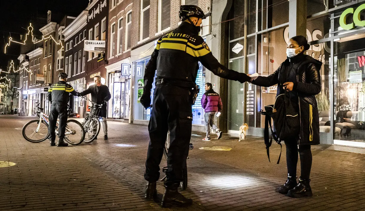Polisi mengontrol sertifikasi keluar pada orang yang lewat saat jam malam dimulai di Haarlem, Belanda (23/1/2021). Belanda memasuki fase terberat dari pembatasan anti-virus Corona hingga saat ini. (AFP/ANP/Koen van Weel)