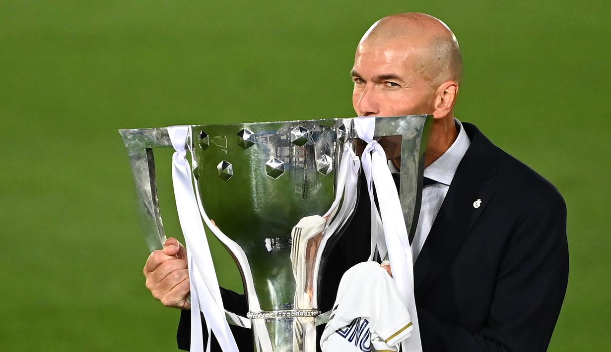 Pelatih Real Madrid, Zinedine Zidane, mengangkat trofi juara La Liga musim 2019/2020 usai timnya mengalahkan Villarreal pada laga lanjutan La liga di Estadio Alfredo Di Stefano, Jumat (17/7/2020) dini hari WIB. (AFP/Gabriel Bouys)