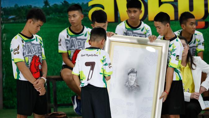 12 anak laki-laki dan pelatih sepak bola mereka, yang diselamatkan dari gua banjir di Thailand, memberi penghormatan terhadap lukisan penyelam AL Thailand yang meninggal selama operasi penyelamatan di Chiang Rai, Rabu (18/7). (AP/Vincent Thian)