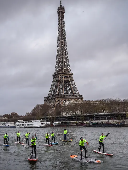 Peserta menyeberangi sungai Seine dekat menara Eiffel selama Nautic Paddle Race di Paris, Minggu (9/12). Sekitar 800 orang mengikuti lomba dayung sambil berdiri terbesar di dunia sejauh 11 km dengan pemandangan kota Paris. (Lucas BARIOULET/AFP)