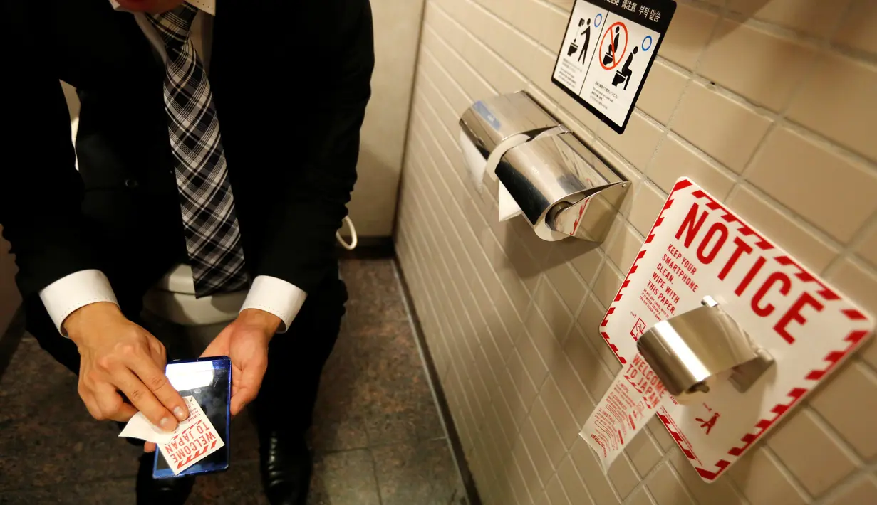 Seorang pria membersihkan ponselnya dengan kertas toilet yang dipasang oleh perusahaan Jepang NTT DoCoMo di kamar mandi berteknologi tinggi yang dilengkapi bidet dan kursi hangat di bandara internasional Narita, Jepang, (28/12). (REUTERS / Toru Hanai)