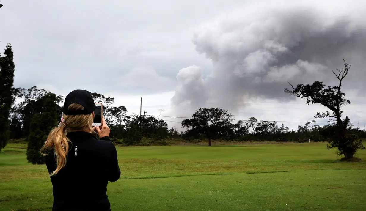 Marie Brant, dari California, mengambil gambar asap tebal yang berembus dari puncak gunung berapi Kilauea di Hawaii. Kamis (17/5). Para wisatawan tetap santai dan justru menjadikan letusan gunung ini sebagai objek wisata. (AP Photo/Caleb Jones)