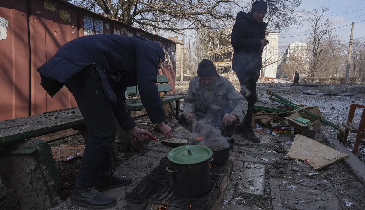 Para pria memasak makanan di sebuah jalan di Mariupol, Ukraina, Minggu, 13 Maret 2022. Rusia melancarkan invasi berskala besar ke Ukraina, salah satu negara tetangganya di sebelah barat daya. (AP Photo/Evgeniy Maloletka)