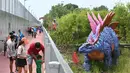 Orang-orang berhenti untuk mengambil foto replika dinosaurus seukuran aslinya yang dipajang di sepanjang "Changi Jurassic Mile" jalan santai di Singapura (13/10/2020). Ada 22 replika dinosaurus yang dibangun di jalur Bandara Changi dengan East Coast Park. (AFP/Roslan Rahman)