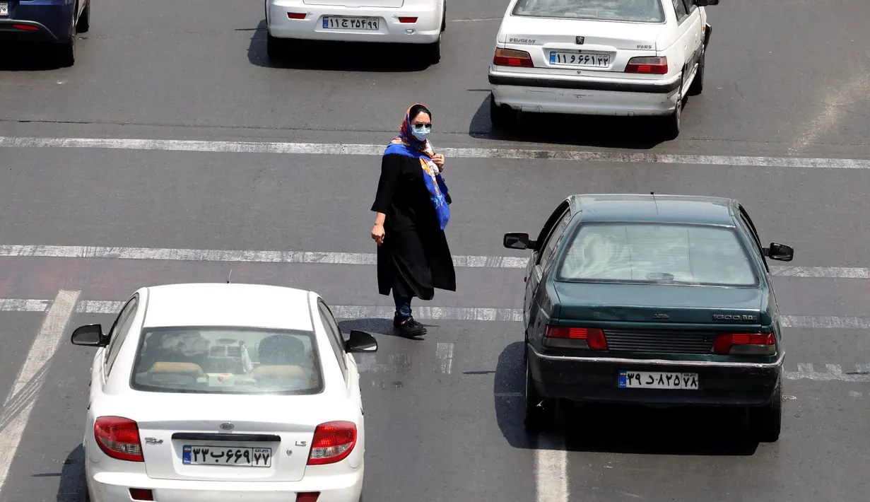 Seorang wanita Iran yang mengenakan masker menyeberang jalan di ibu kota Teheran, Sabtu (3/7/2021). Presiden Hassan Rouhani mengaku khawatir Iran akan dilanda gelombang kelima pandemi Covid-19 karena kemunculan virus corona varian Delta. (ATTA KENARE/AFP)