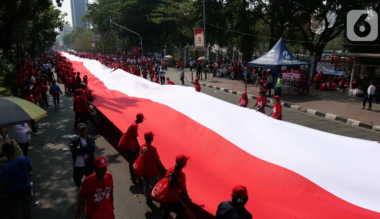 Sejumlah relawan membentangkan Bendera Merah Putih di kawasan jalan Medan Merdeka Selatan, Jakarta, Minggu (20/10/2019). Bendera Merah Putih Sekitar 200 meter dibentangkan jelang pelantikan Presiden-Wapres RI terpilih Joko Widodo-Ma'ruf Amin periode 2019-2024. (Liputan6.com/Herman Zakharia)