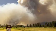 Tanda selamat datang di Greenville terlihat di depan kepulan asap yang mengepul saat api Dixie membakar dekat kota Greenville, California (3/8/2021). Api Dixie telah membakar lebih dari 250.000 hektar dan terus mendekati komunitas perumahan. (AFP/Josh Edelson)