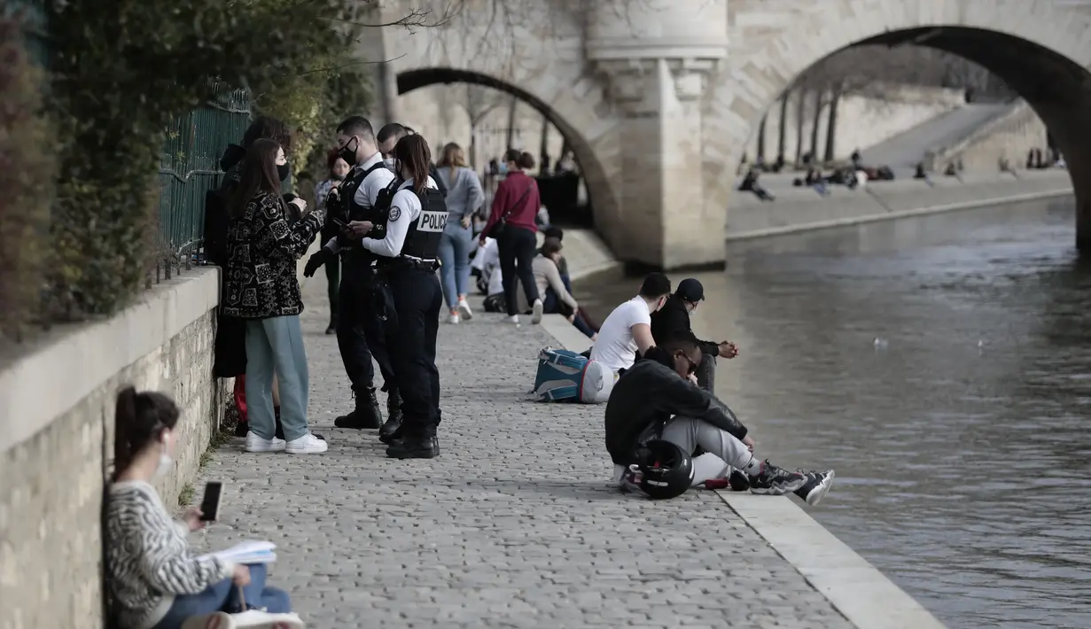 Petugas polisi memeriksa dokumen ketika orang-orang berjalan di sepanjang tepi sungai Seine di Paris, Rabu (3/3/2021).  Tingkat infeksi COVID-19 tetap tinggi selama beberapa minggu, dan pasien virus menempati 70% unit perawatan intensif negara itu. (AP Photo/Lewis Joly)