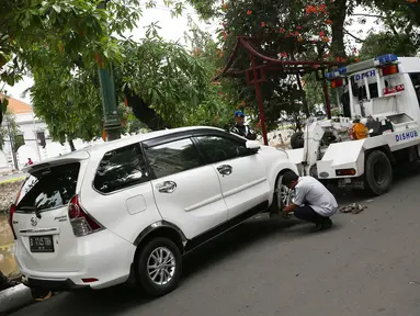 Petugas Dinas Perhubungan mengaitkan kendaraan pada mobil derek di kawasan Pasar Baru, Jakarta, Kamis (14/12). Meskipun sering ditertibkan, namun masih banyak pengendara yang nekat parkir sembarangan. (Liputan6.com/Immanuel Antonius)