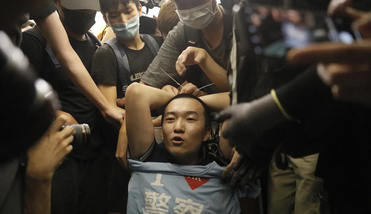 Para pengunjuk rasa mengikat seorang pria yang mengenakan kaus bertuliskan kata-kata "Saya suka polisi" yang menurut para pengunjuk rasa adalah seorang petugas polisi dari China daratan, saat demonstrasi di Bandara di Hong Kong (13/8/2019). (AP Photo/Vincent Yu)