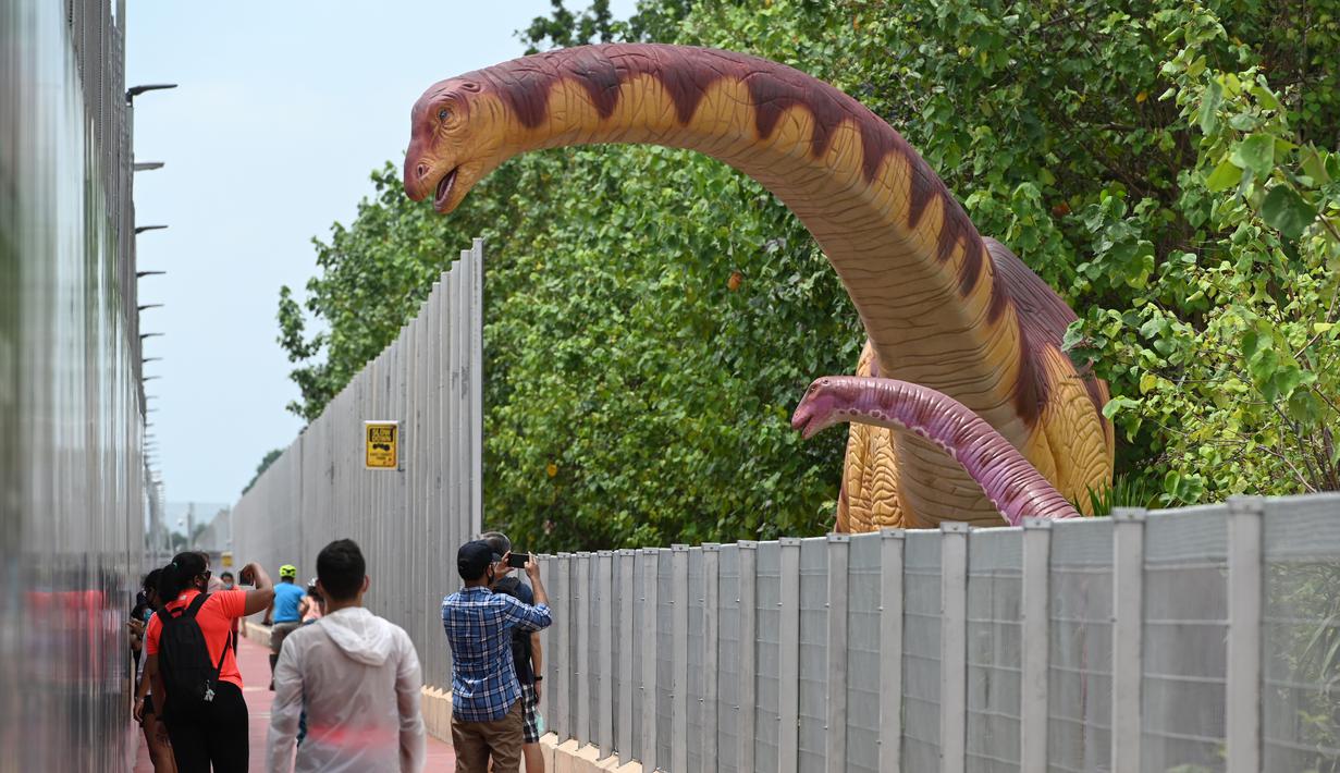 Orang-orang berhenti untuk mengambil foto replika dinosaurus seukuran aslinya yang dipajang di sepanjang "Changi Jurassic Mile" jalan santai di Singapura (13/10/2020). Singapura membangun replika-replika dinosaurus di jalur menunju bandara Changi. (AFP/Roslan Rahman)