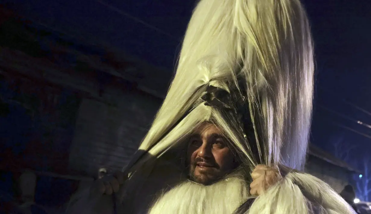 Penari bertopeng melihat melalui rambut topengnya saat ritual kuno mengusir roh jahat di jalan-jalan Batanovci, Bulgaria, Kamis (13/1/2022). Setiap musim dingin di desa-desa seluruh negara Balkan, warga mengenakan topeng ritual dan kostum melakukan tarian di sekitar api unggun. (AP/Valentina Petrova