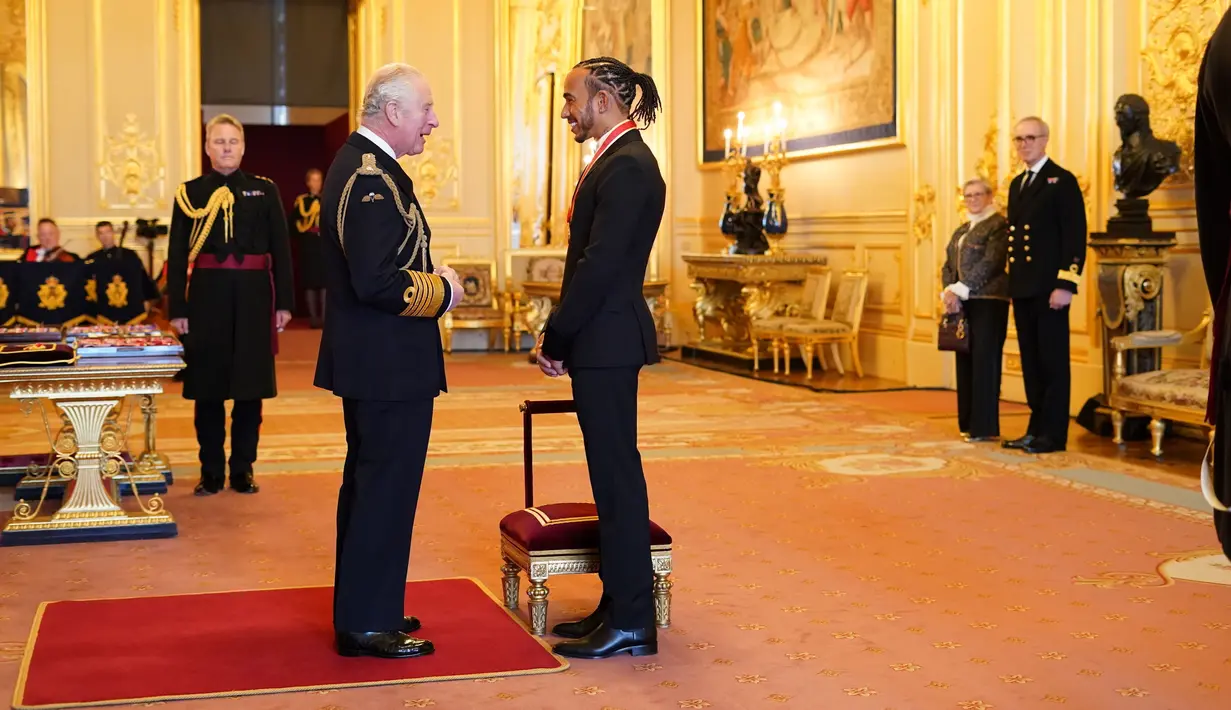 Pembalap Lewis Hamilton berbincang dengan Pangeran Charles setelah menerima gelar kebangsawanan dari Kerajaan Inggris di Kastil Windsor, Rabu (15/12/2021). Sebelumnya Lewis telah menerima gelar kebangsawanan Member of British Empire atau MBE pada 2009. (Dominic Lipinski/PA via AP)