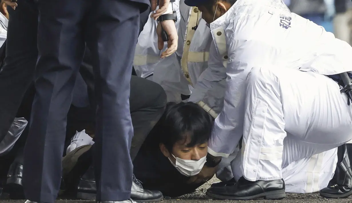 Rekaman NHK menunjukkan beberapa petugas polisi berseragam dan berpakaian preman berkumpul di sekitar pria tersebut, menekannya ke tanah dan menyeretnya ke samping. (Kyodo News via AP)