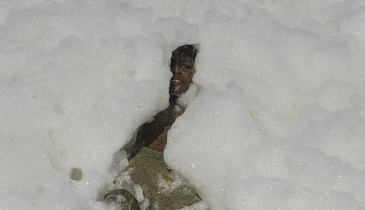Seorang anak berendam di limbah busa yang disebabkan polutan saat bercampur dengan ombak di pantai di Chennai (29/11/2019). Untuk kedua kalinya dalam sebulan, pantai-pantai Chennai ditutupi limbah busa, sekitar 7 km bentangan pantai dari Foreshore Estate ke Tiruvanmiyur. (AFP/Arun Sankar)