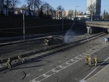 Tentara Ukraina berjalan di dekat puing-puing truk militer yang terbakar di sebuah jalan di Kyiv, Ukraina, Sabtu (26/2/2022). Pasukan Rusia menyerbu ke arah ibukota Ukraina Sabtu, dan pertempuran jalanan pecah saat pejabat kota mendesak penduduk untuk berlindung. (AP Photo/Efrem Lukatsky)