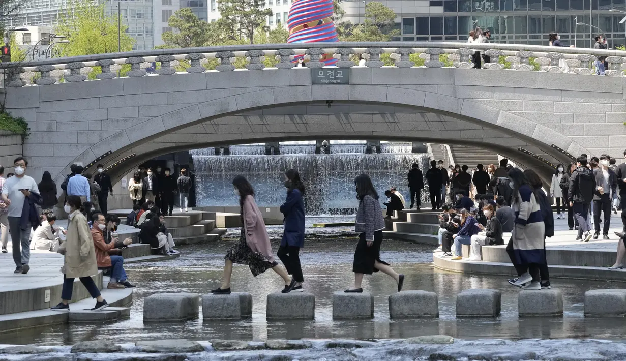 Orang-orang yang memakai masker menyeberangi Sungai Cheonggye di Seoul, Korea Selatan, Jumat (15/4/2022). Korea Selatan atau Korsel akan menghapus sebagian besar pembatasan pandemi covid-19, termasuk batas berkumpul di dalam ruangan, mulai 18 April 2022. (AP Photo/Ahn Young-joon)
