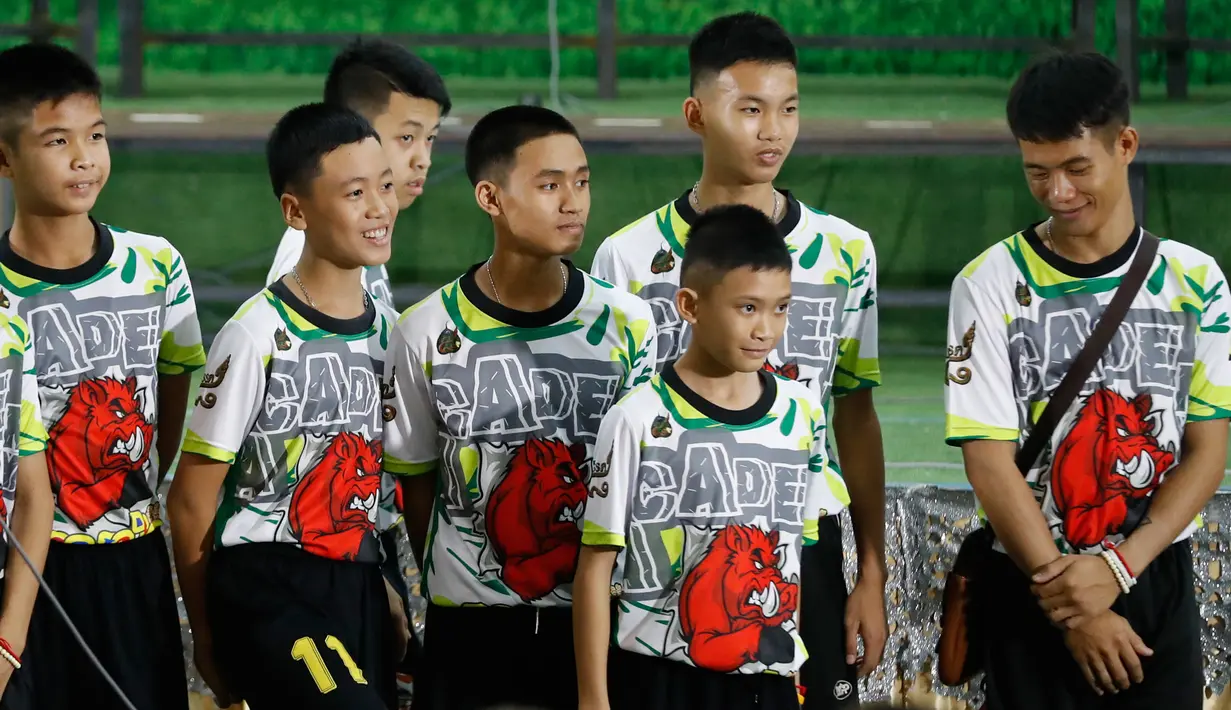 12 anak laki-laki dan pelatih sepak bola mereka, yang diselamatkan dari gua banjir di Thailand tampil ke muka publik untuk pertama kalinya di Chiang Rai, Rabu (18/7). Mereka memasuki ruang konferensi pers dengan memakai seragam. (AP/Vincent Thian)