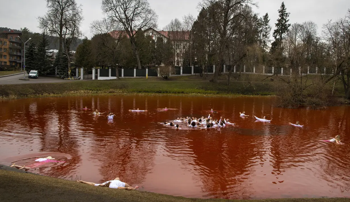Orang-orang mandi dalam kolam warna merah untuk menandakan darah selama protes di depan kedubes Rusia di Vilnius, Lithuania, Kamis (7/4/2022). Pejabat Ukraina mengatakan 410 jasad warga sipil ditemukan di kota-kota wilayah Kiev yang baru-baru ini direbut kembali. (AP Photo/Mindaugas Kulbis)