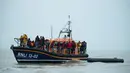 Para migran berdiri di atas sekoci RNLI (Royal National Lifeboat Institution) setelah diselamatkan saat menyeberangi Selat Inggris di lepas pantai di Dungeness, Inggris tenggara (24/11/2021). (AFP/Ben Stansall)