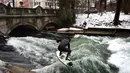 Aksi peselancar menaklukkan ombak saat berselancar di Sungai Eisbach selama hari musim dingin di Munich, Jerman, 4 Januari 2017. Tidak hanya peselancar lokal namun turis pun tertantang untuk mencoba berselancar di sungai kota Munich.  (Mark RALSTON/AFP)