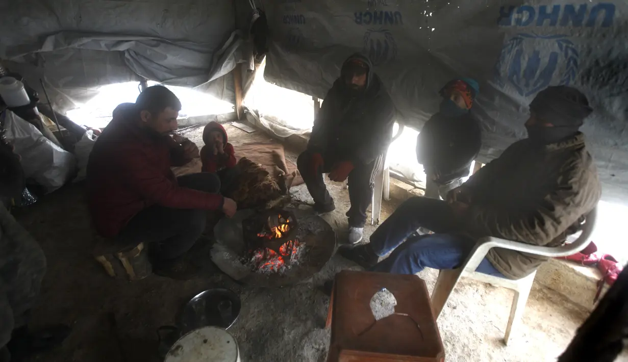 Pengungsi Suriah menghangatkan diri di sekitar api di dalam tenda di sebuah kamp pengungsi dekat Zahrani, Lebanon, pada 19 Januari 2022. Beberapa membakar pakaian tua, plastik, dan bahan berbahaya lainnya agar tetap hangat saat suhu turun dan kemiskinan melonjak. (AP Photo/Mohammed Zaatari)