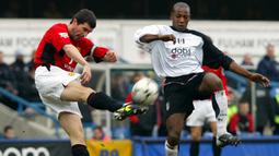 Gelandang Manchester United, Roy Keane (kiri) berusaha membuang bola dari ancaman striker Fulham, Luis Boa Morte pada laga Liga Inggris 2003/2004 di Loftus Road, London (28/2/2004). Roy Keane yang total membela Manchester United selama hampir 13 musim mulai 1993/1994 hingga tengah musim 2005/2006, didatangkan Setan Merah dari Nottingham Forest yang harus terdegradasi pada akhir musim 1992/1993. MU mengeluarkan mahar sebesar 8,5 juta euro untuk sang pemain yang total tampil 478 laga dengan torehan 51 gol dan 38 assist. (AFP/Adrian Dennis)