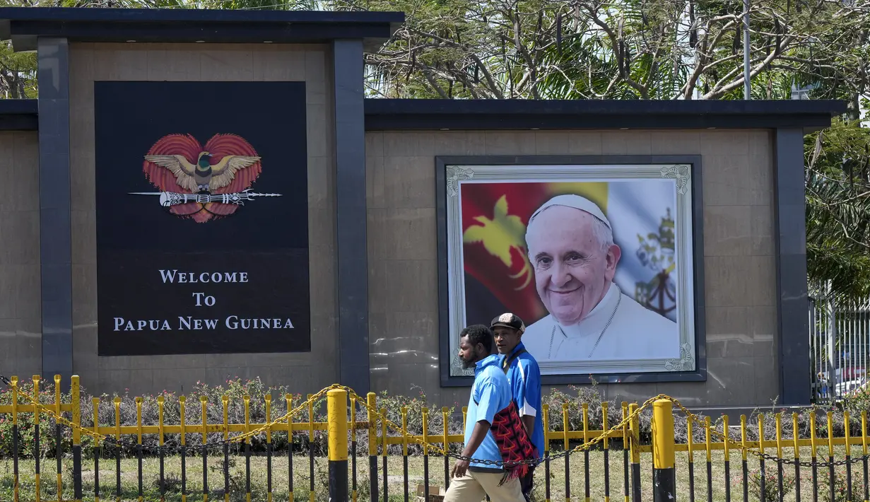 Warga setempat berjalan melewati foto Paus Fransiskus jelang kunjungannya ke Port Moresby, Papua Nugini, Rabu (4/9/2024). (AP Photo/Mark Baker)