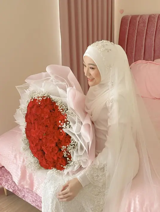 Larissa tampil cantik  mengenakan busana pengantin putih-putih.  Perempuan seorang anak itu tampak tersenyum bahagia duduk sambil memegang buket bunga mawar merah berukuran besar. [Instagram/larissachou]