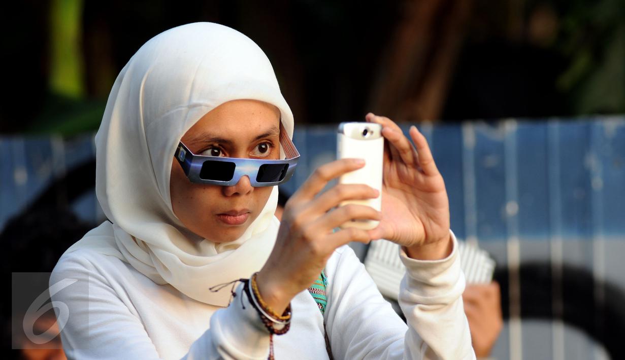 Warga menggunakan kamera telepon selular untuk mengabadikan proses gerhana matahari di sekitar Taman Ismail Marzuki, Jakarta, Rabu (9/3/2016). Di Jakarta, fenomena gerhana matahari 90% bisa diamati selama 2,11 menit. (Liputan6.com/Helmi Fithriansyah)   