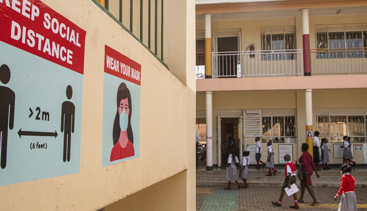 Murid-murid berjalan melewati poster dinding yang menyerukan protokol kesehatan Covid-19 di Sekolah Dasar Nalya pada hari pertama pembukaan kembali di Kampala, 10 Januari 2022. Sekolah-sekolah di Uganda dibuka kembali, mengakhiri penutupan sekolah terlama di dunia akibat COVID-19 (Badru KATUMBA/AFP)
