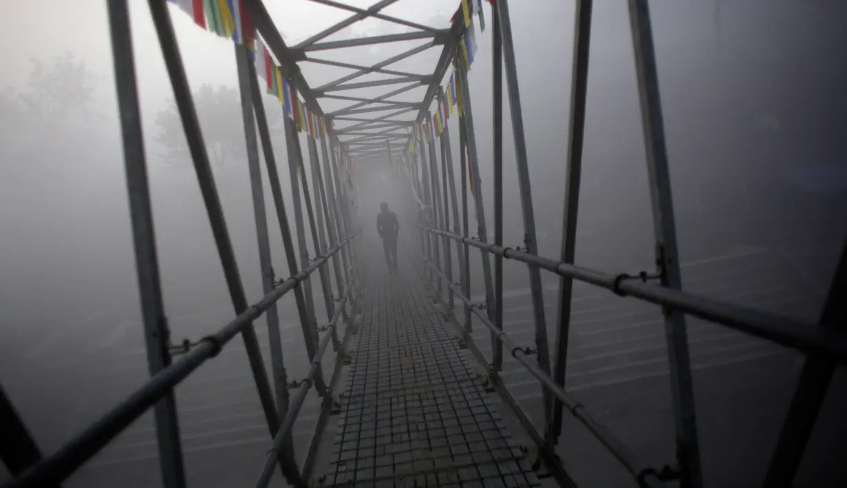 Seorang pria Nepal menyusuri jembatan untuk mengikuti ritual selama festival Gaya Aunsi di Kathmandu, Nepal (21/12). Walau diselimuti kabut tebal mereka tetap menggelar ritual suci tersebut. (AP Photo/Niranjan Shrestha)