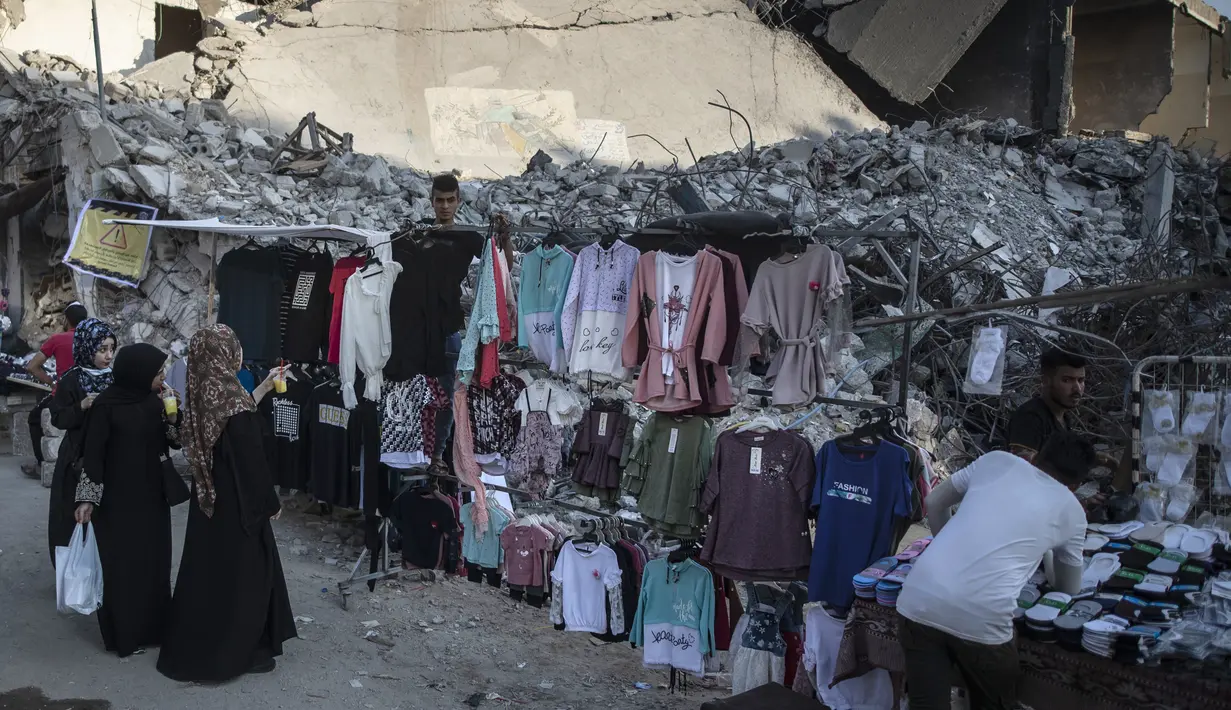 Pedagang kaki lima Palestina memajang pakaian untuk dijual di samping puing-puing bangunan di Kota Gaza, Minggu (18/7/2021). Bagi warga Palestina yang kehilangan orang-orang terkasih dalam pertempuran antara militan Gaza dan Israel, tidak ada alasan untuk merayakan Idul Adha. (AP Photo/Khalil Hamra)