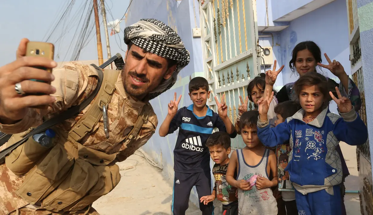 Seorang anggota pasukan Peshmerga berselfie dengan sejumlah anak-anak usai berhasil merebut kembali desa Fadiliya dari ISIS di Nawaran, Mosul, Irak (27/10). (REUTERS/Air Jalal)