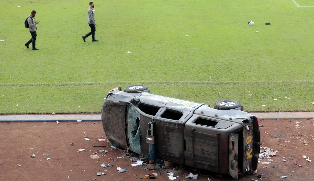 Petugas berjalan melewati mobil polisi yang rusak dalam tragedi kerusuhan pada pertandingan sepak bola antara Arema Vs Persebaya di Stadion Kanjuruhan Malang, Jawa Timur, Minggu (2/10/2022). Sejumlah kendaraan terlihat terguling di dalam di Stadion Kanjuruhan. (AP Photo/Trisnadi)