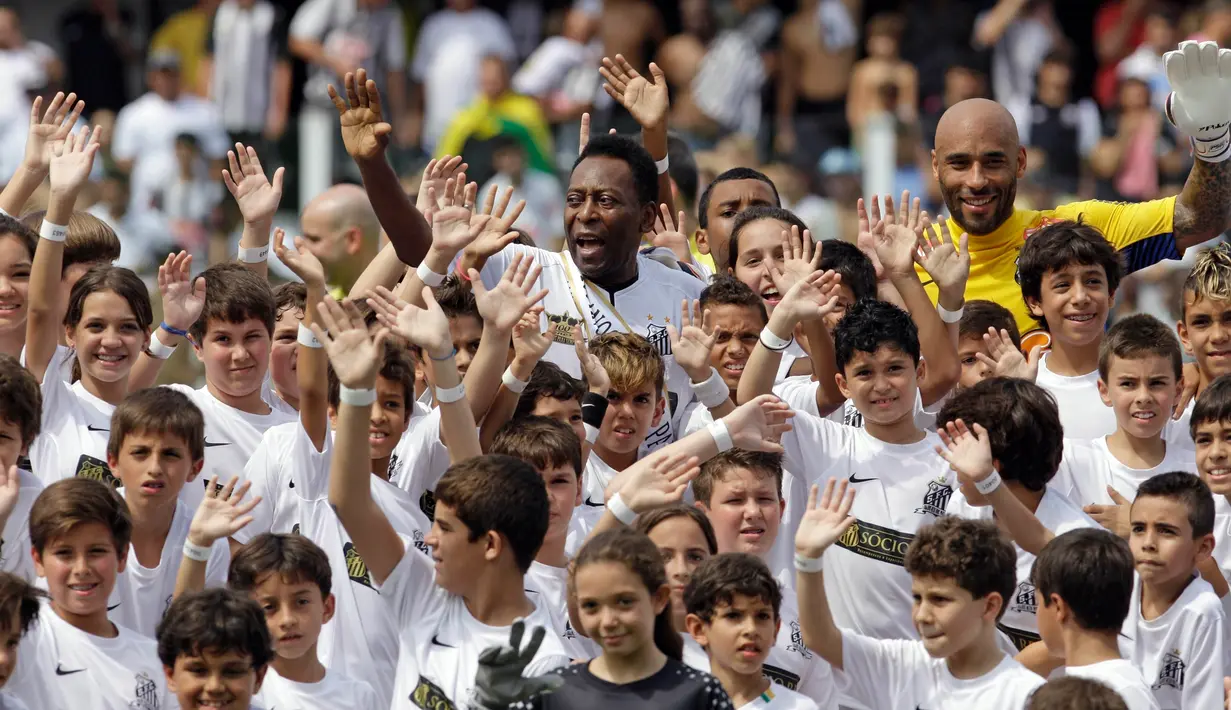 Legenda sepak bola Brasil Pele (tengah atas) dan putranya Edson Cholbi do Nascimento (kanan atas) melambai bersama anak-anak selama perayaan ulang tahun keseratus tim di Santos, Brasil, 14 April 2012. Dalam perjalanan kariernya, Pele telah mempesona dunia dengan kejeniusannya dalam olahraga, menghentikan perang, melakukan kerja sosial di seluruh dunia dan menyebarkan apa yang paling dia yakini sebagai obat untuk semua masalah kita: cinta. (AP Photo/Nelson Antoine, File)