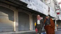 Warga Palestina berjalan melewati toko-toko yang tutup di kota Nablus, Tepi Barat, (7/12). Usai Presiden AS, Donald Trump mengumumkan Yerusalem sebagai ibu kota Israel suasana sepi terlihat di kawasan tersebut. (AFP Photo/Hazem Bader)