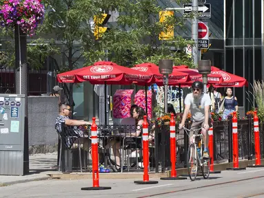 Pengendara sepeda melewati area makan terbuka sebuah restoran di Toronto, Kanada, 18 Juli 2020. Kota Toronto meluncurkan program CafeTO yang memungkinkan restoran dan bar memperluas area makan terbuka mereka guna melayani lebih banyak pelanggan dengan aman selama pandemi COVID-19. (Xinhua/Zou Zheng)